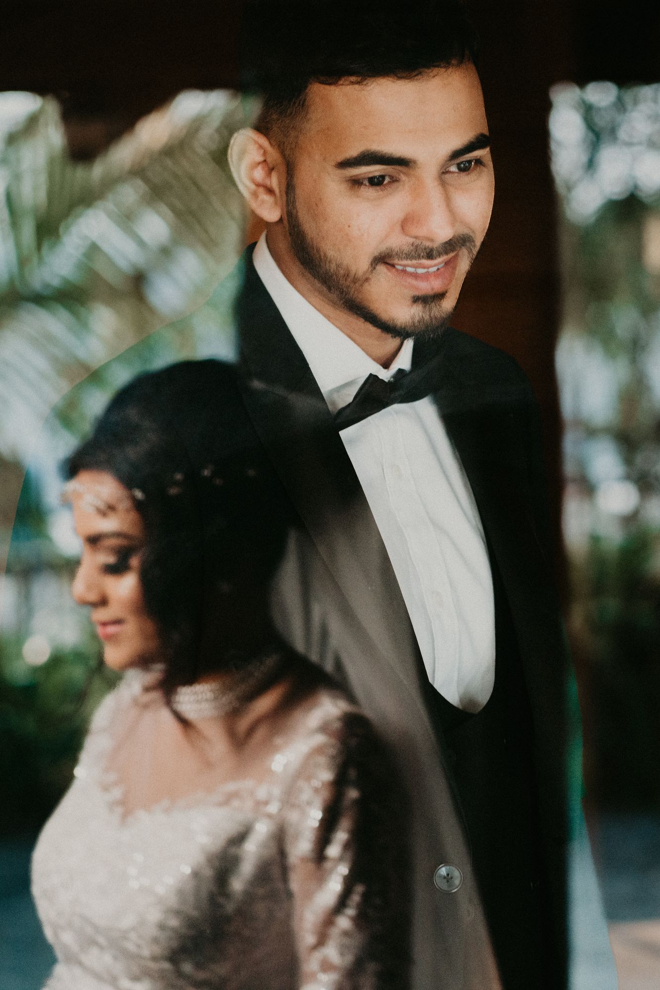 A groom in a tuxedo smiling over his bride's shoulder