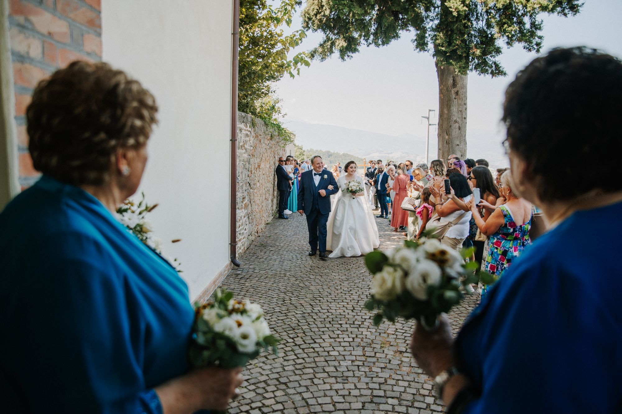 Guests holding bouquets as the couple walk a cobbled lane